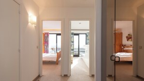A hotel corridor with two bedrooms, each with a bed and a nightstand. The corridor has a carpeted floor and a white wall. - Apartment in Middelkerke With Sea View (Middelkerke)
