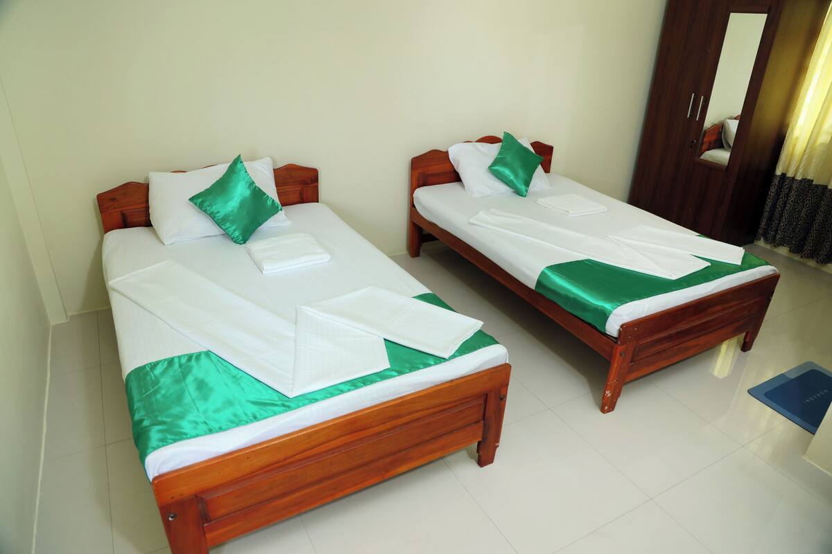 Two wooden beds with green and white bedding, a wooden wardrobe, and a mirror.