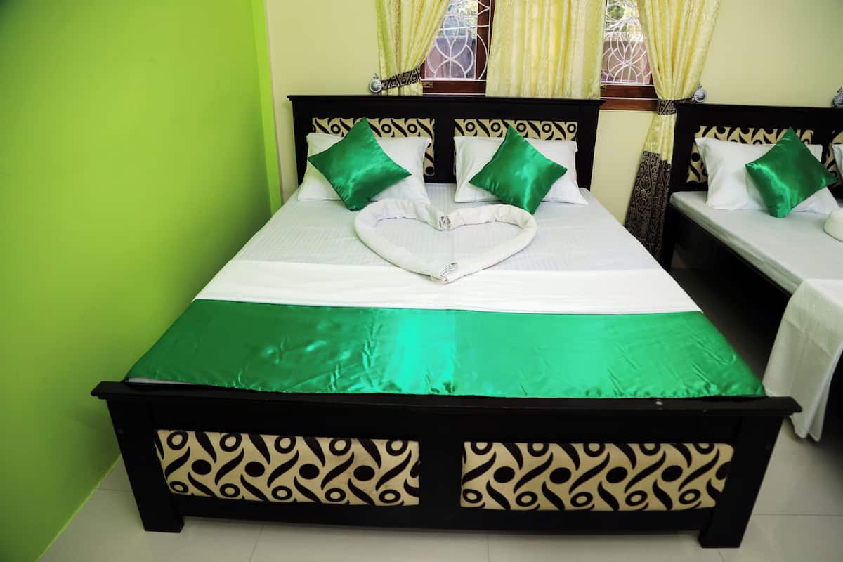 A neatly made bed with green and white bedding, two green pillows, and a heart-shaped towel.