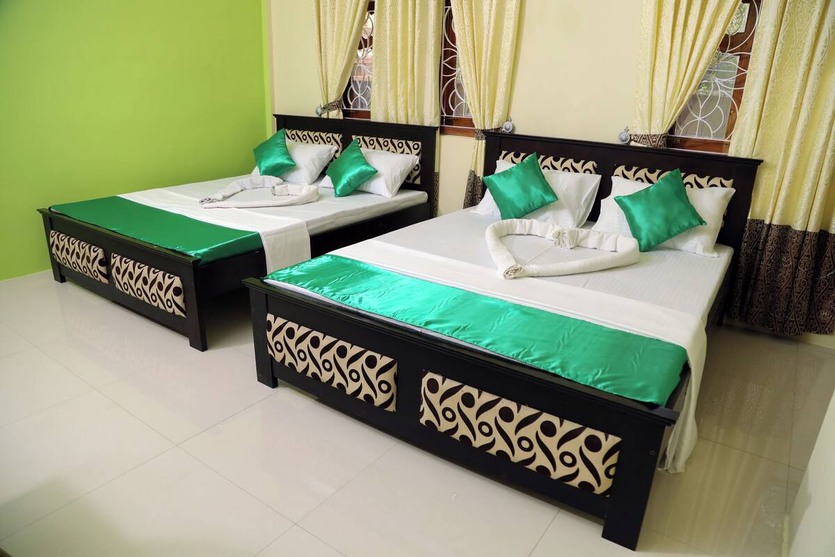 Two single beds with green bedspreads and white pillows, a black headboard with a decorative pattern, and a green wall.
