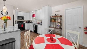 A modern kitchen with white cabinets, a black stove, and a dining area with a red and white table.