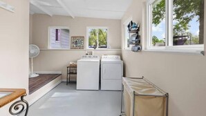 A laundry room with two washing machines, a drying rack, and a window with a view of trees.