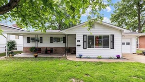A single-story house with a front porch, a brick foundation, and a small front yard with grass and potted plants.
