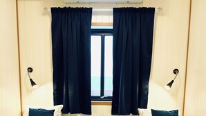 Huoneessa on kaksi sänkyä, pieni pöytä ja ikkuna, jossa on verhot.