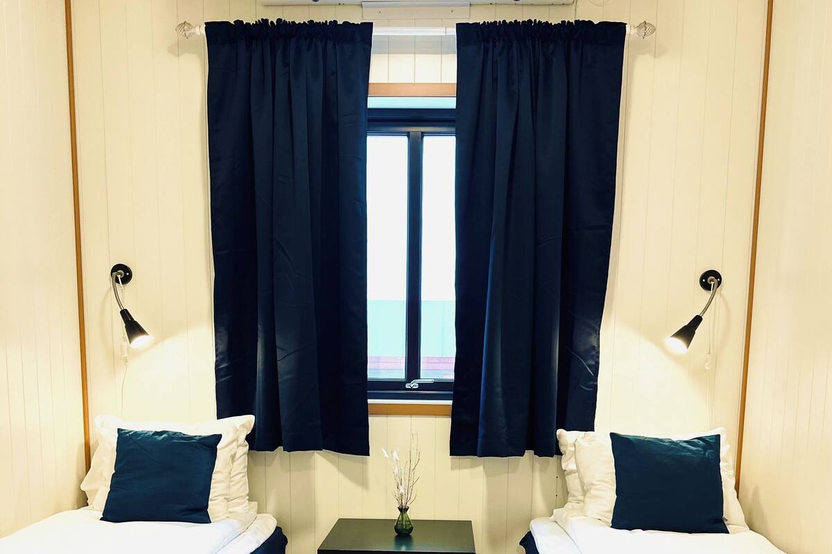 A room with two beds, a small table, and a window with curtains.
