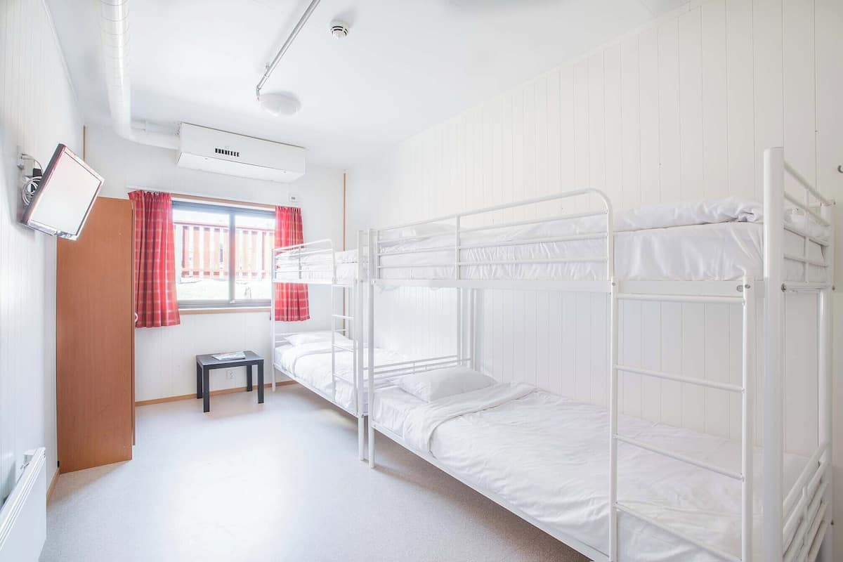 A bunk room with two beds, a small table, a window with red curtains, and an air conditioning unit.