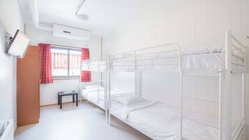 Dormitorio con literas, una mesita pequeña, una ventana con cortinas rojas y un equipo de aire acondicionado.