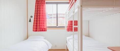 Ein Schlafsaalzimmer mit Etagenbetten, einem Fenster mit roten Vorhängen und einem Lüftungsgitter an der Decke.