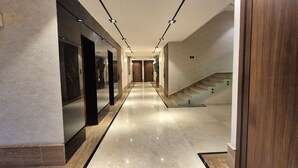 A modern hotel corridor with a polished marble floor, a wooden staircase, and a series of doors and mirrors. - Qurtoba big apartment all yours (Riyadh)