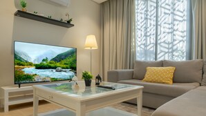 A modern living room with a flat-screen TV, a glass coffee table, a sofa, and a lamp. - Qurtoba big apartment all yours (Riyadh)