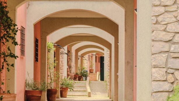 Un estrecho callejón con arcos, plantas en macetas y un muro de piedra.
