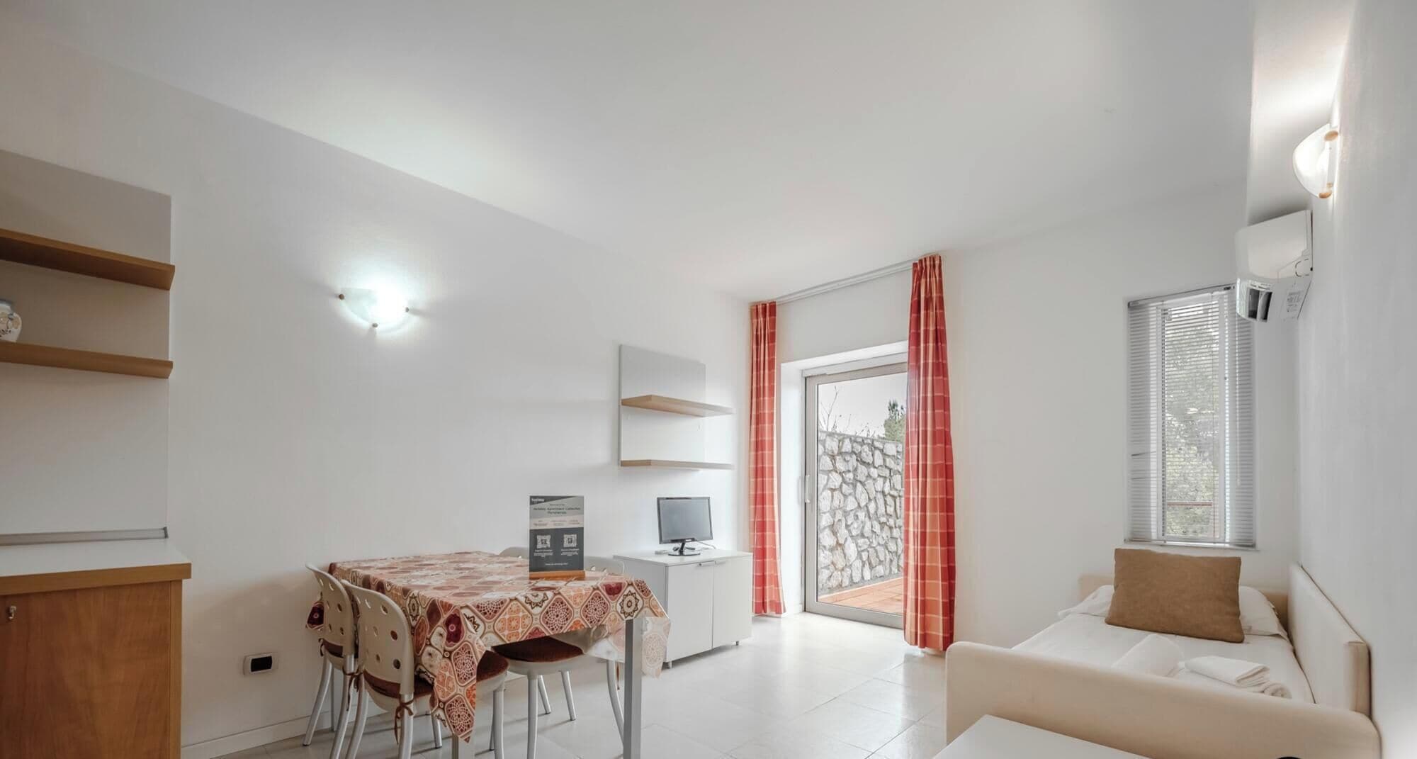 Ein modernes Wohnzimmer mit einer Couch, einem Esstisch mit Stühlen, einem Fernseher und einer Küchenzeile mit Kühlschrank.