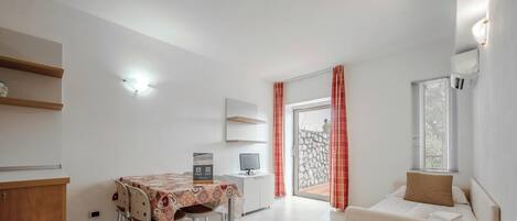 Una sala de estar moderna con un sofá, una mesa de comedor con sillas, un televisor y una zona de cocina con un refrigerador.