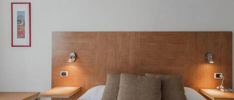 A hotel room with a wooden headboard, two bedside tables, a bed with white bedding, and a framed picture on the wall.