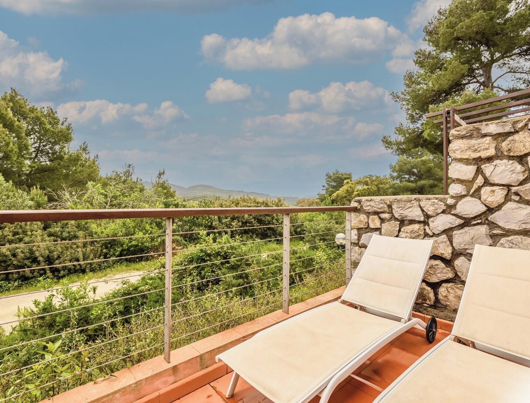 Un balcone con due lettini, un muro in pietra e vista su un paesaggio montuoso.