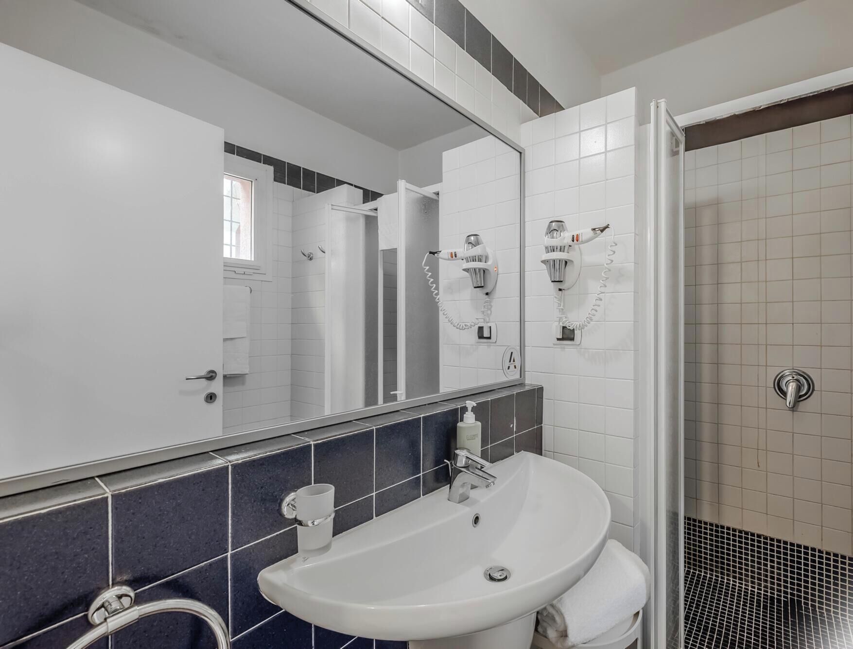 Un baño con lavamanos blanco, un espejo y cabina de ducha.