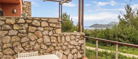 A patio with a stone wall, a white table, and chairs, overlooking a coastal landscape.