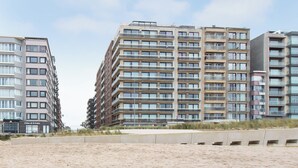 Un hotel frente al mar con varios pisos, balcones y una playa arenosa en primer plano.