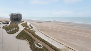 Una estructura arquitectónica moderna con un diseño esférico distintivo, ubicada junto a una playa bajo un cielo despejado.