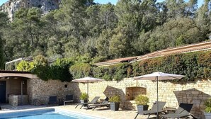 A pool area with lounge chairs and umbrellas, surrounded by stone walls and vegetation. - Le Mas de San lou (Cabasse)