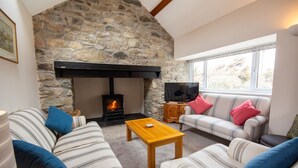 A cozy living room with a stone fireplace, striped sofas, and a television. - Ty'r Garreg - sleeps 7 guests  in 4 bedrooms (Rhoscolyn)