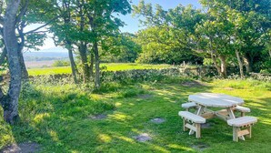 A picnic table in a grassy area with trees and a stone wall in the background. - Ty'r Garreg - sleeps 7 guests  in 4 bedrooms (Rhoscolyn)