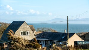 A coastal house with a stone exterior, a sloped roof, and a view of the sea and distant mountains. - Ty'r Garreg - sleeps 7 guests  in 4 bedrooms (Rhoscolyn)
