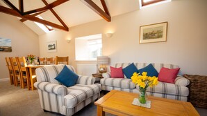 A living room with striped sofas, a wooden coffee table, and a dining area with chairs and a table. - Ty'r Garreg - sleeps 7 guests  in 4 bedrooms (Rhoscolyn)