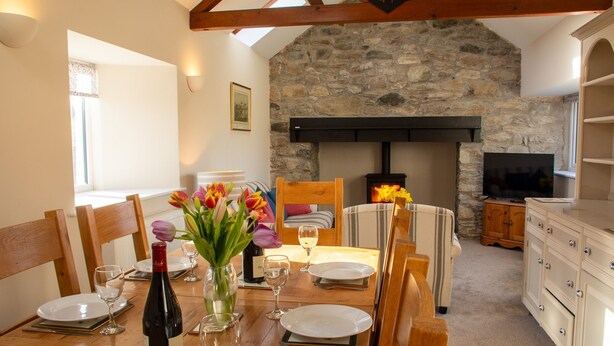 A dining area with a stone wall, wooden beams, a fireplace, and a television in the background. - Ty'r Garreg - sleeps 7 guests  in 4 bedrooms (Rhoscolyn)