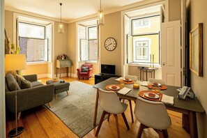 Una sala de estar moderna con un sofá, una mesa de comedor para dos personas y un televisor.