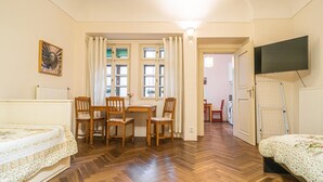 A room with a wooden herringbone floor, a dining table with four chairs, a bed with a floral bedspread, a radiator, and a television on the wall. - 1 Bed Flat - Sleeps 4 - Pets - Wifi (Prague)