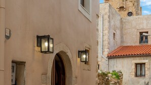 A narrow alleyway with a building entrance featuring an arched doorway, stone walls, and a potted plant. - Golden Theros villa,Village Experiene in Maroulas (Maroulas)