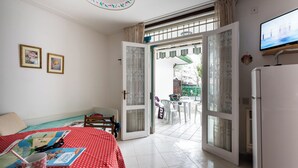 A room with a bed, a table with a red polka dot tablecloth, a map, and a mug. There is a TV on the wall and a refrigerator. - Luminous Apartment With Garden (San Michele al Tagliamento)
