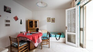 A dining area with a table set for two, a wooden cabinet, and a sofa with a cushion. - Luminous Apartment With Garden (San Michele al Tagliamento)