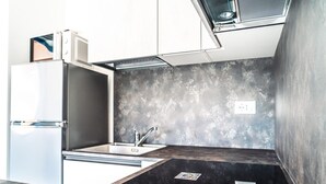 Cocina compacta con microondas integrado, un lavamanos y encimera negra.