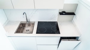 A modern kitchen with a stainless steel sink, black induction cooktop, white cabinets, and a black countertop. - Beautiful Flat With sea View in Bibione (San Michele al Tagliamento)