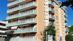 A multi-story residential building with balconies, a sign indicating a nearby center, and a clear blue sky.