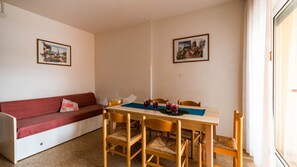 A cozy room with a red sofa, a wooden dining table with four chairs, and two framed pictures on the walls. - Bright Flat Just Steps From Bibione Beach (San Michele al Tagliamento)
