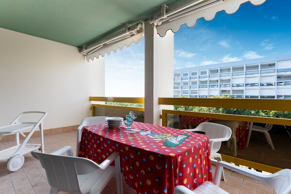 A balcony with a table set for dining, white chairs, and a view of a building.