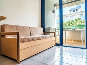 A wooden sofa with a woven cover in a room with a tiled floor and a sliding glass door leading to an outdoor balcony. - Cozy Apartment With Sunny Terrace in Bibione (San Michele al Tagliamento)