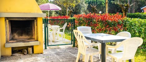 Un patio al aire libre con una parrilla, sillas de plástico blanco y una mesa.