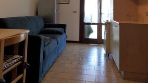 A living room with a sofa, a ceiling fan, a television, and a kitchen area with cabinets. - Flat With Parking Only 100m From the Beach (San Michele al Tagliamento)