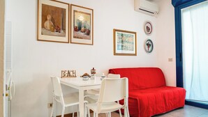 A room with a white table, four white chairs, a red sofa, and three framed artworks on the wall. - Beachside Elegant Studio for Four Guests (San Michele al Tagliamento)