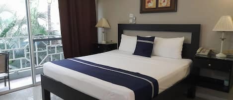 A hotel room with a bed, a nightstand, a lamp, a picture frame, and a window with curtains.