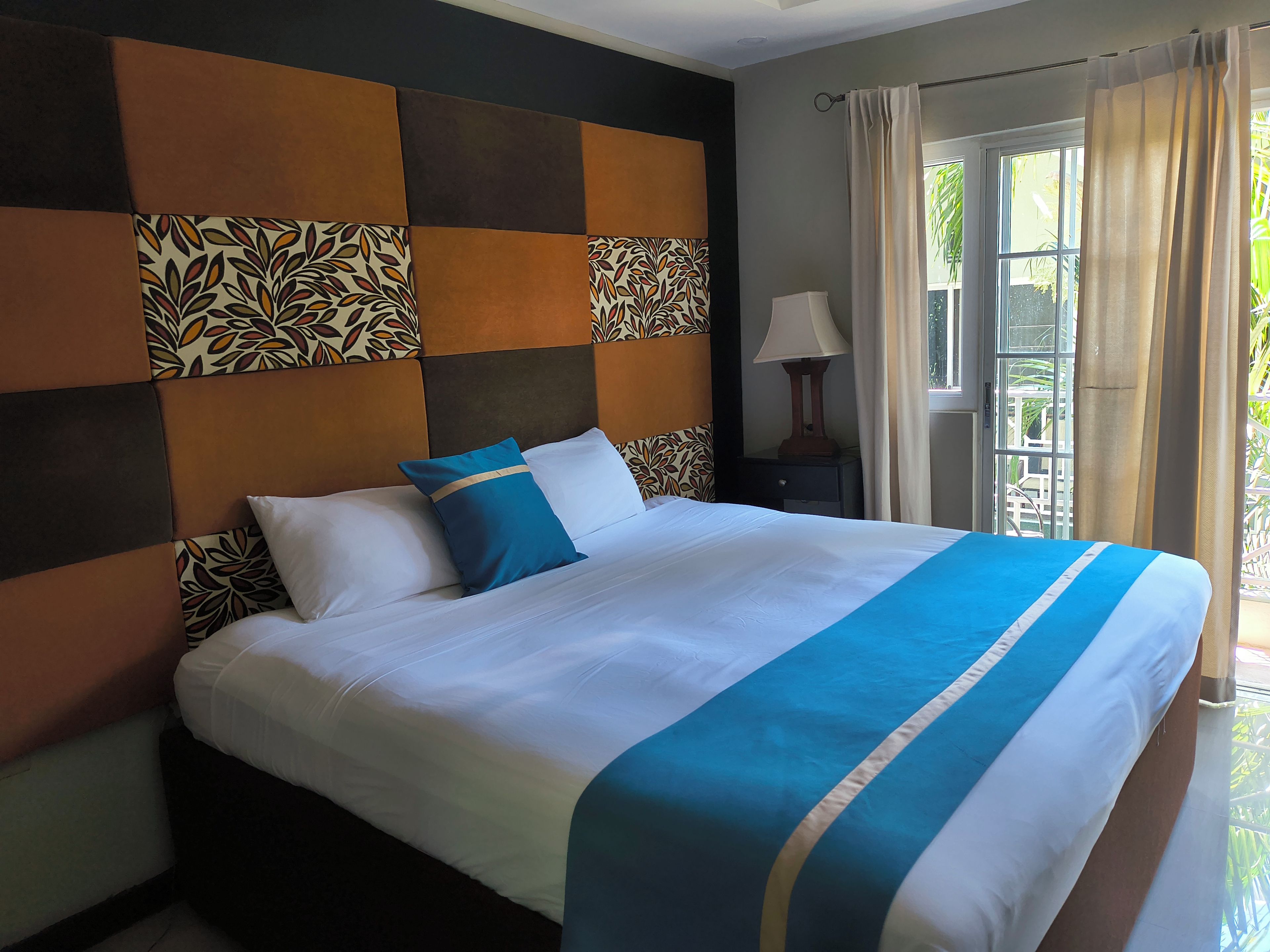 Uma cama com cabeceira estampada, uma luminária de cabeceira e vista para o exterior pela janela.