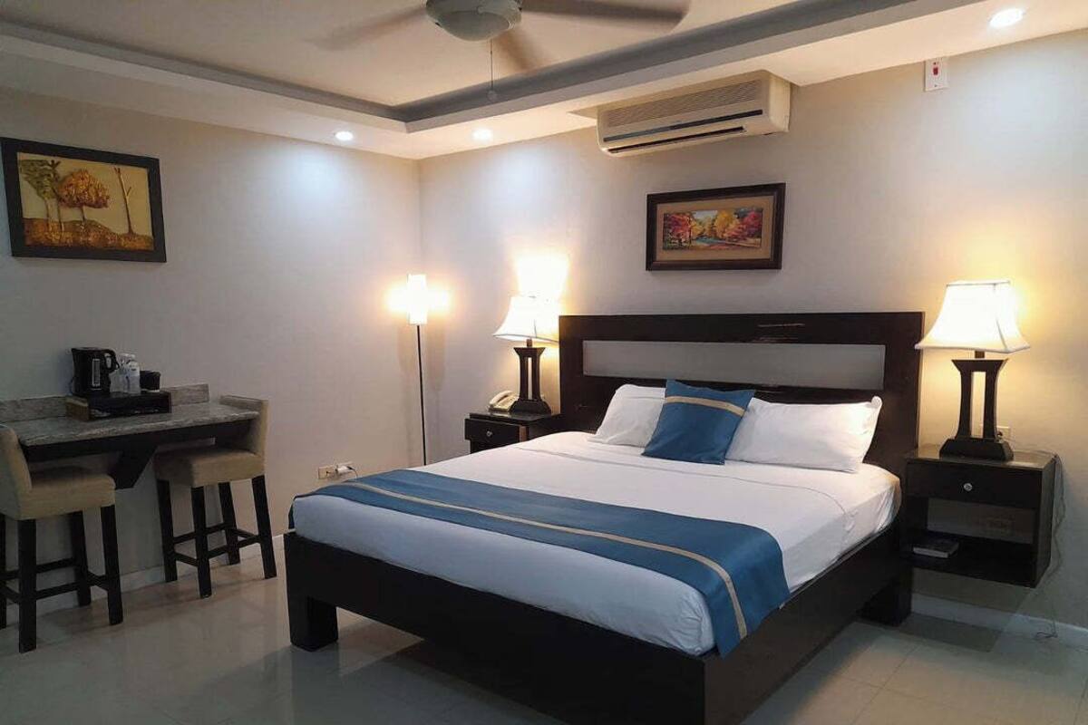 Une chambre d’hôtel équipée d’un lit, d’un bureau, de chaises, de lampes et d’œuvres d’art accrochées aux murs.