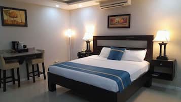 A hotel room with a bed, desk, chairs, lamps, and artwork on the walls.
