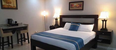 A hotel room with a bed, desk, chairs, lamps, and artwork on the walls.