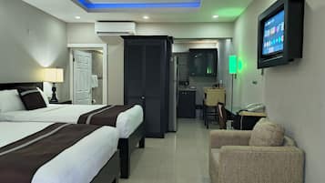 Una habitación de hotel con dos camas, un escritorio con silla, televisor y kitchenette.