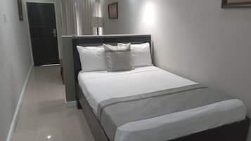 Una cama bien hecha con ropa de cama blanca y un detalle en gris, una lámpara de noche y un cuadro en la pared.